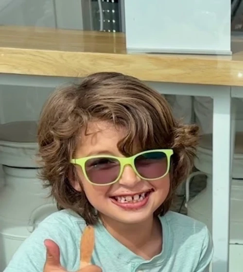 The reference photo: a child with curly hair and yellow-green sunglasses, giving a thumbs up