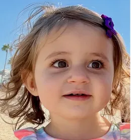 Lyric, a toddler with big brown eyes, curly hair, and a purple flower clip